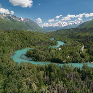 Large blue river running through a vast canyon with snow capped mountains and lush greenery