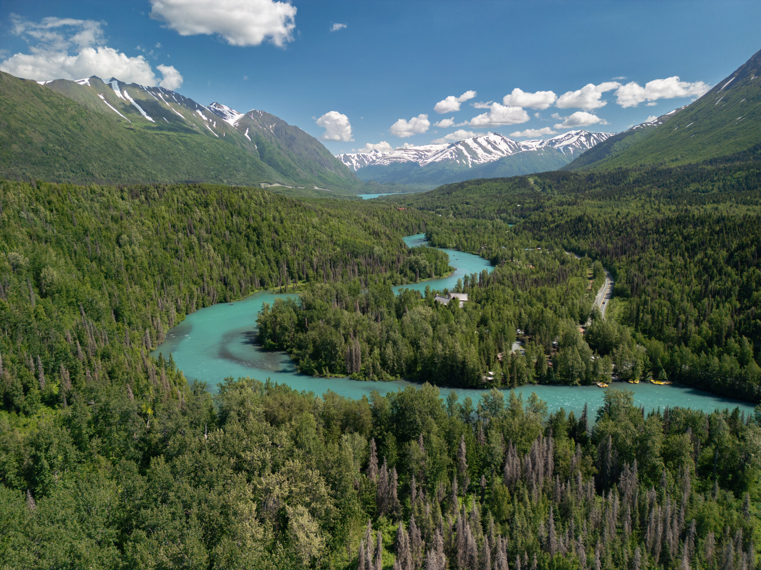 Large blue river running through a vast canyon with snow capped mountains and lush greenery